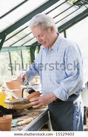 Man in greenhouse putting soil in pot smiling