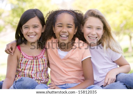 Three young girl friends sitting outdoors smiling