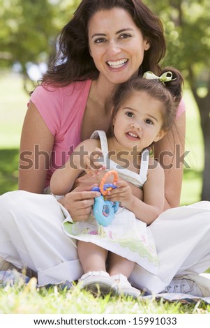 Woman and young girl sitting outdoors with toy smiling