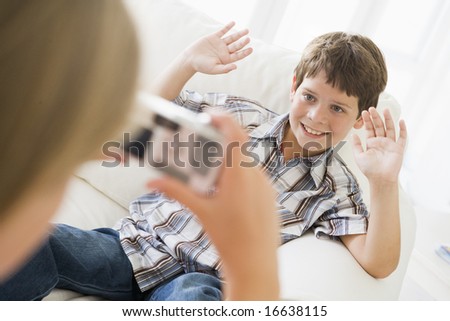 Young girl taking picture of smiling young boy with camera phone indoors