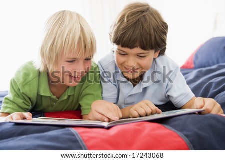 Two Young Boys Lying Down On A Bed Reading A Book