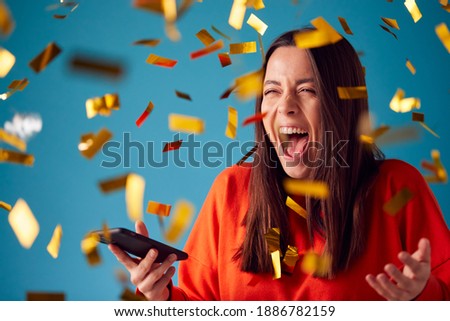 Celebrating Young Woman With Mobile Phone Winning Prize And Showered With Gold Confetti In Studio