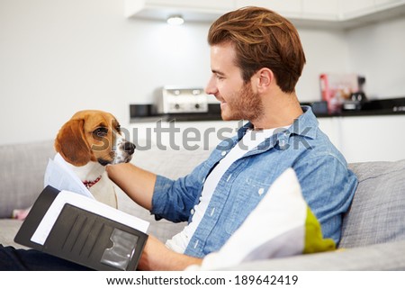 Man Looking At Paperwork And Playing With Pet Dog At Home