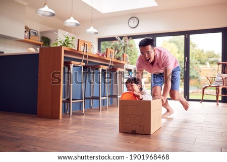Asian Father And Son Pushing Son Around Kitchen Floor At Home In Junk Modelled Car