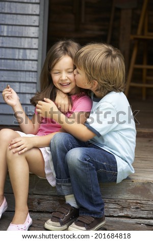 Young boy kissing sister on veranda