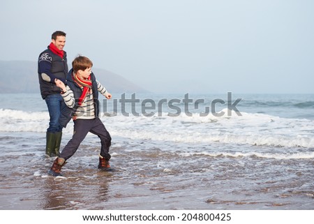 Father And Son Walking On Winter Beach And Throwing Stones