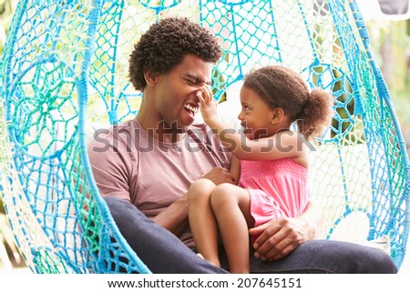 Father With Daughter Relaxing On Outdoor Garden Swing Seat