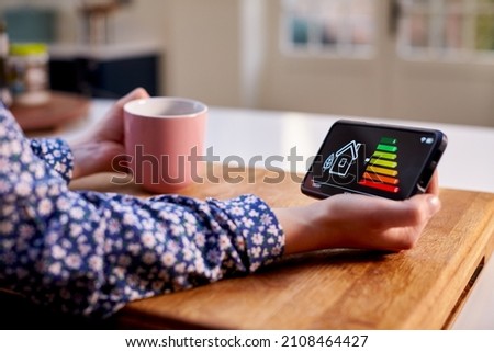 Close Up Of Woman Holding Smart Energy Meter In Kitchen Measuring Energy Efficiency 商業照片 © 