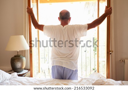 Rear View Of Man Waking Up In Bed In Morning