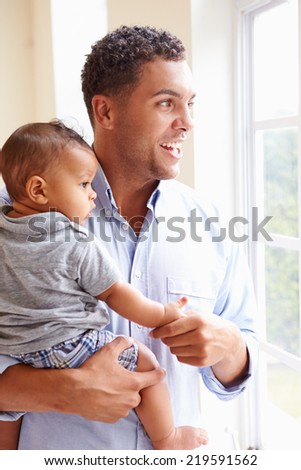 Smiling Father Standing By Window With Baby Son At Home
