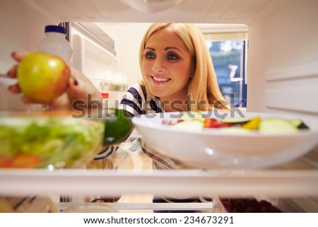 Woman Looking Inside Fridge Full Of Food And Choosing Apple
