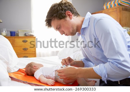 Father Dressed For Work Changing Baby\'s Diaper In Bedroom