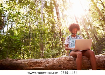 Woman Sits On Tree Trunk In Forest Using Laptop Computer