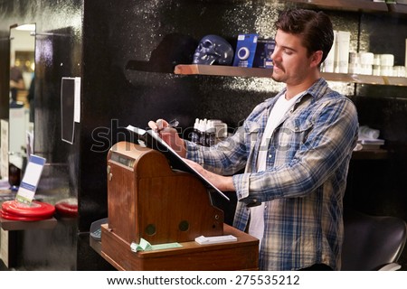 Male Barber Standing By Cash Register Writing Down Booking