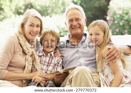 Portrait Of Grandparents Reading To Grandchildren On Sofa