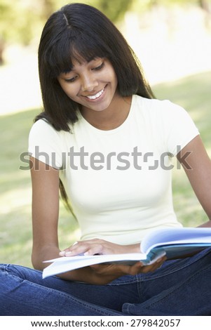 Female College Student Sitting In Park Reading Textbook