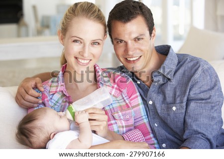 Young Family With Baby Feeding On Sofa At Home