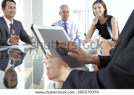 Close Up Of Businesswoman Using Tablet Computer During Board Meeting Around Glass Table