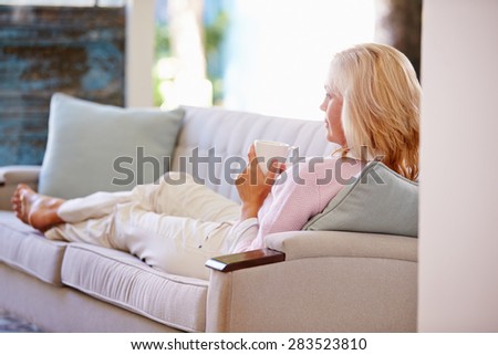 Mature Woman Relaxing On Sofa At Home Watching Television
