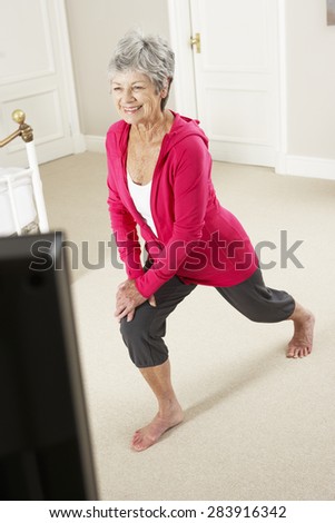 Senior Woman Exercising Whilst Watching Fitness DVD On Television