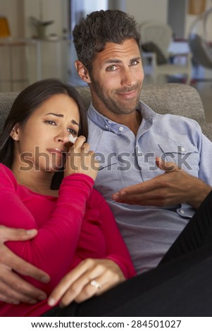 Hispanic Couple On Sofa Watching Sad Movie On TV