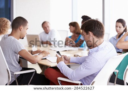 Businessman Using Mobile Phone In Boardroom Meeting