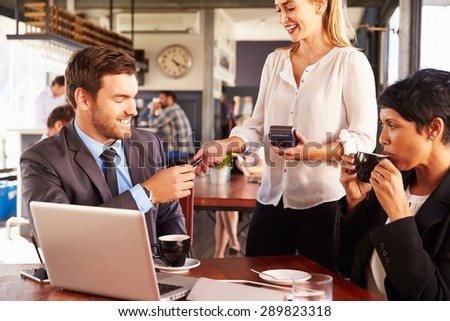 Two business people with laptop paying in a coffee shop