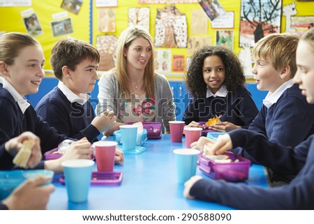 Schoolchildren With Teacher Sitting At Table Eating Lunch