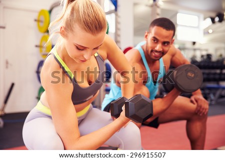 Man and woman exercising with dumbbells at a gym
