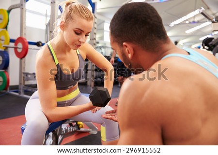 Woman weight training at a gym getting advice from a trainer