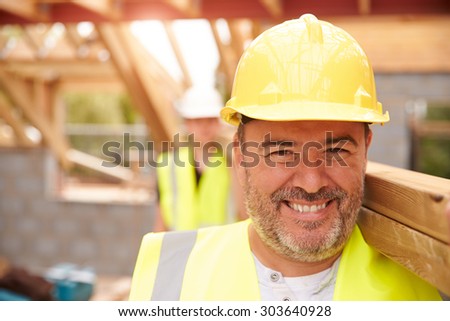 Builder And Apprentice Carrying Wood On Construction Site