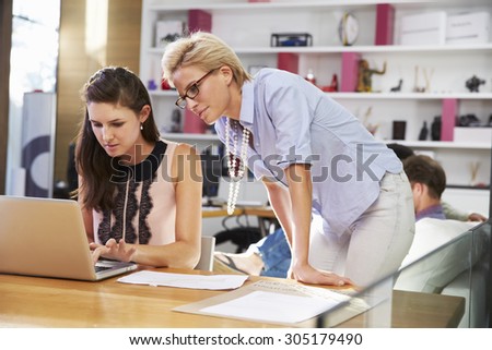 Two Businesswomen Working On Laptop In Busy Office