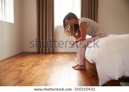 Woman Suffering From Depression Sitting On Bed And Crying