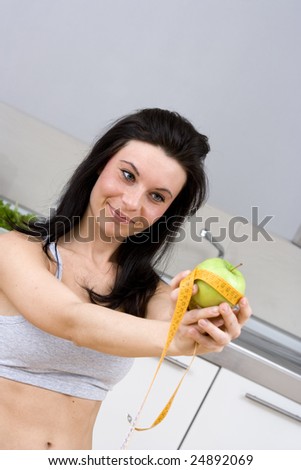 young caucasian woman with black hairs measure apple with a flexible centimeter to show  how slim will became with an healthy diet.Shooted in kitchen