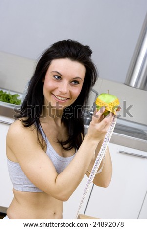 young caucasian woman with black hairs measure apple with a flexible centimeter to show  how slim will became with an healthy diet.Shooted in kitchen