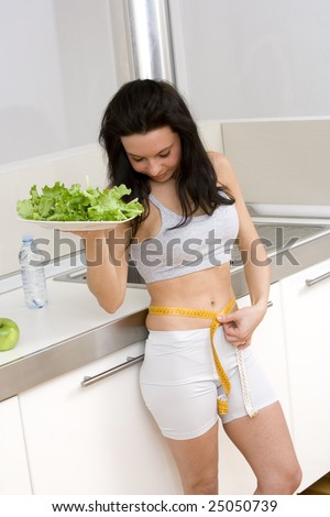 young caucasian brunette in kitchen with a sald dish and a centimeter to measure her hips.Concept of correct food to have a slim body
