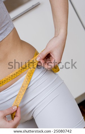 close up oblique view of a woman measuring her hips ,with gym wear.Concept of control of diet