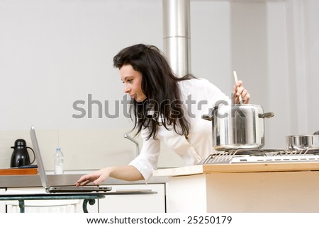 young caucasian brunette working with laptop while cooking in her kitchen.Concept of online receipt,hard working.