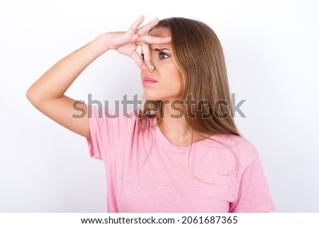Displeased Young Caucasian girl wearing pink T-shirt on white background plugs nose as smells something stink and unpleasant, feels aversion, hates disgusting scent. Imagine de stoc © 