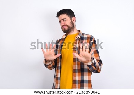 Afraid young caucasian man wearing plaid shirt over white background, makes terrified expression and stop gesture with both hands saying: Stay there. Panic concept. Foto stock © 