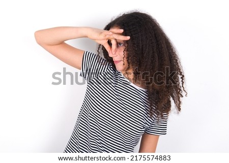 Displeased young beautiful brunette woman wearing striped t-shirt over white wall plugs nose as smells something stink and unpleasant, feels aversion, hates disgusting scent. Imagine de stoc © 