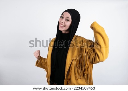Attractive young beautiful muslim woman wearing hijab and yellow jacket over white background celebrating a victory punching the air with his fists and a beaming toothy smile Foto stock © 