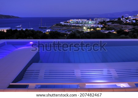 swimming pool and open air balcony in night illumination at the modern luxury hotel with Aegean Sea as background, Crete, Greece