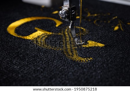 Machine embroidery on black velvet fabric with yellow thread. Embroidered initial G. Close up.