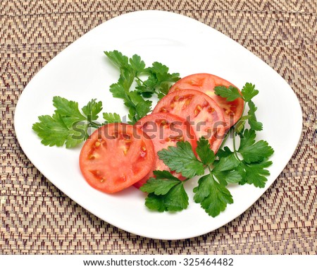 Fresh parsley and succulent sliced tomatoes on a white plate on a wicker background