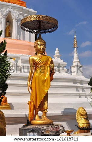 CHIANG MAI, THAILAND:  Standing gilded statue of the Buddha shaded by a metal parasol in front of the great white Chedi at Wat Changkam at Wiang Kum Kam Ancient Village