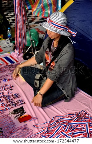 Bangkok, Thailand January 16, 2014:  Thai woman sitting cross-legged on Silom Road selling a variety of Operation Shut Down Bangkok red, white, and blue souvenirs