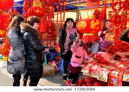 Pengzhou, China January 22, 2014:  A little girl reaches out to touch a big red lantern at a vendor\'s booth selling Chinese New Year decorations