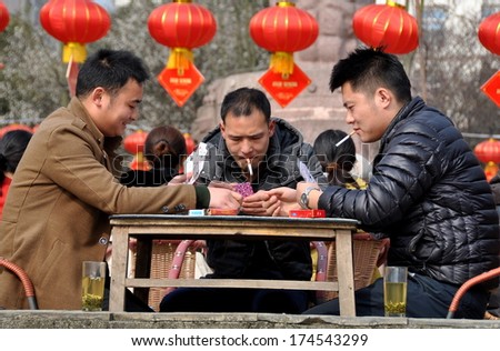 Pengzhou, China February 1, 2014: Three men smoking cigarettes, drinking tea, seated at a table in Pengzhou Cityni Park playing a game of cards