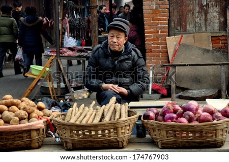 Pengzhou, China, January 29, 2014:  An elderly Chinese man sitting on a stool selling potatoes, onions, and other produce at the Long Xing outdoor marketplace